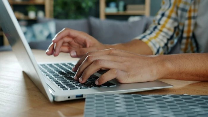 Hands typing on a laptop keyboard at a home desk